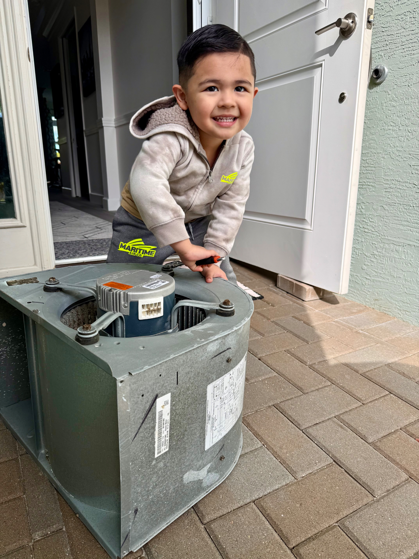 Melice toddler in a Maritime Air Co. hoodie working on a blower assembly